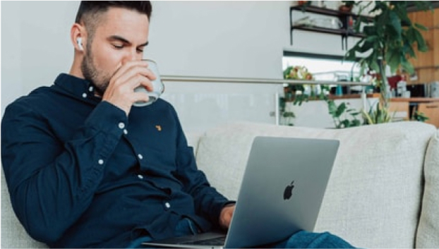 写真：ソファの上で足を伸ばしながらパソコンを触っている男性