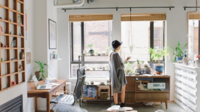 写真：白を基調にした部屋に木材の家具と立っている女性